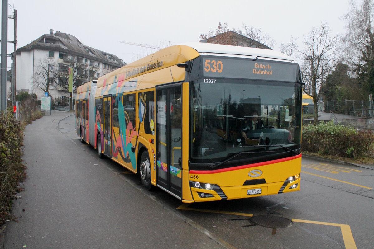Postauto/Regie Zürcher Unterland Nr. 456/PAG-ID: 12327/ZH 670 885  ''E-Mobilität statt Emission'' (Solaris New Urbino 18 Electric) am 14.12.2025 beim Bhf. Bülach. Die Regie Zürcher Unterland nahm zum Fahrplanwechsel 7 Solaris Elektrobusse für die Linien 530 und 531 in Betrieb. Der Wagen Nr. 456 erhielt dazu einen speziellen Anstrich.
