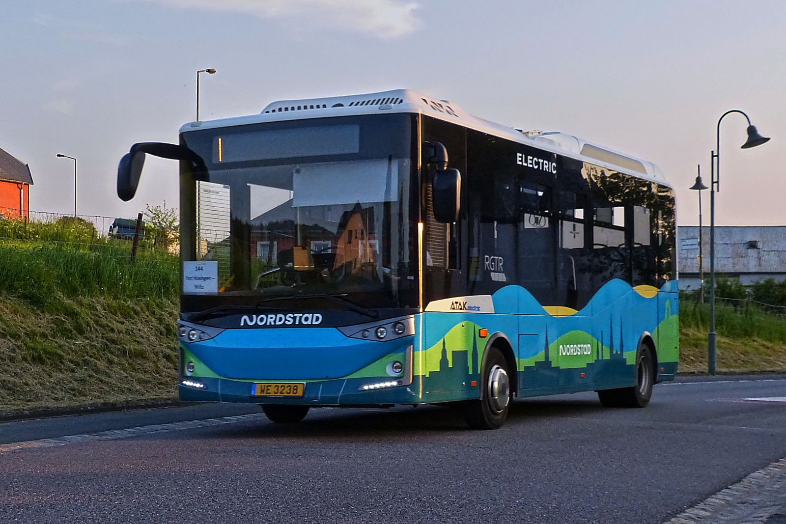 WE 3238, Karsan Atak von WEmobility  bedient die Linie 144 Wiltz – Parc Hosingen, fährt im Abendlicht nahe Wiltz an mir vorbei. 05.2023